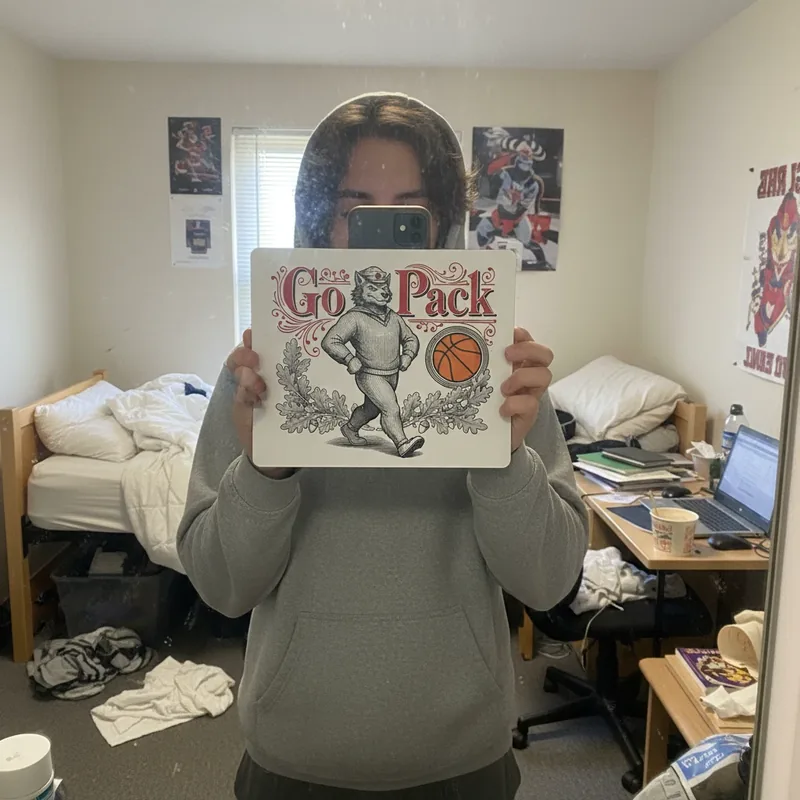 NC State Go Pack mouse pad with a vintage wolf mascot, held up in a dorm room.